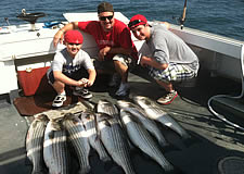 Eight striped bass laid on deck of boat with two boys and dad, the fishermen