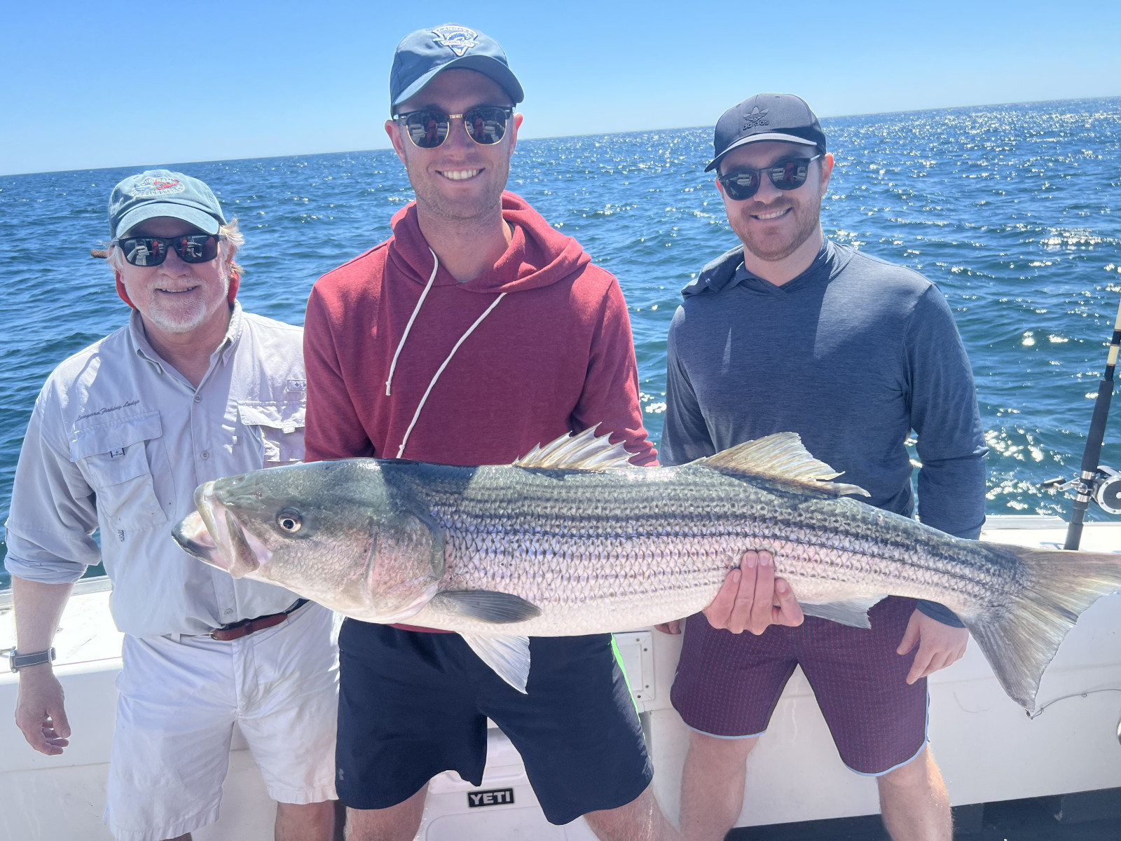 Man holding very very large striped bass, smiling, on deck of the charter fishing boat on a sunny day