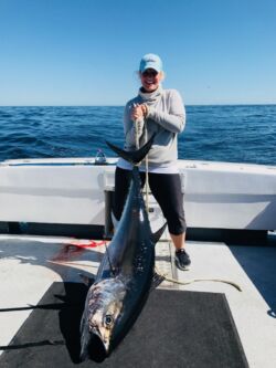 Smiling woman in cap holding up tail of large bluefin tuna