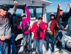 Five smiling men and women, each holding fishing line with striped bass on the end