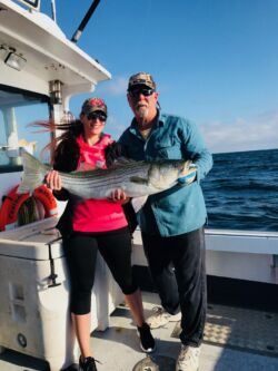 Smiling woman and captain holding large striped bass that she caught