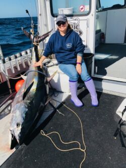 Woman with hand on large bluefin tuna that she caught on rod and reel