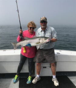 Charter captain and older woman customer with big smile holding large striped bass
