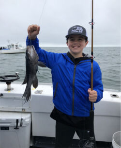 Smiling boy holding up sea bass and fishing rod