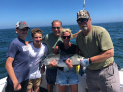 Smiling parents and two children with captain holding a large bass tuna on deck of F/V Magic