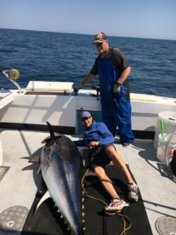 Man lying down beside 6.5 foot bluefin tuna tuna on deck of F/V Magic