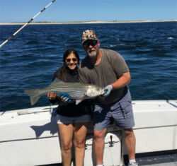 Small woman smiling and holding a large striped bass she caught